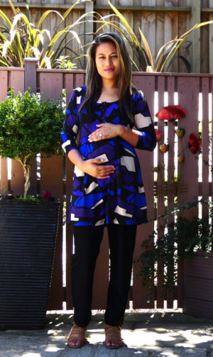 A pregnant model wears a blue patterned tunic top with three quarter sleeves